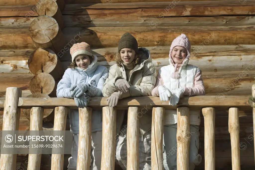 Three preteen or teen girls standing on deck of log cabin, looking away, low angle view