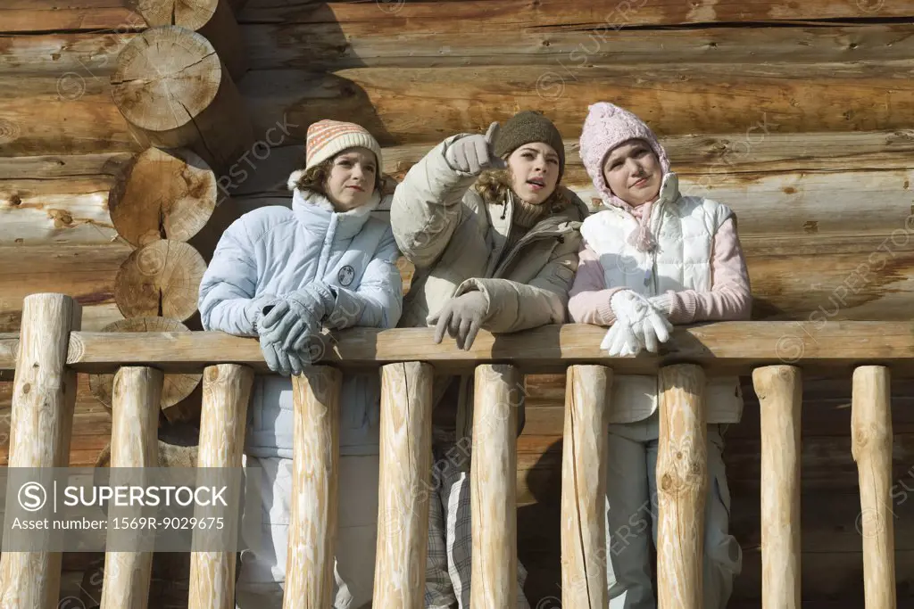 Three preteen or teen girls standing on deck of log cabin, looking away, low angle view