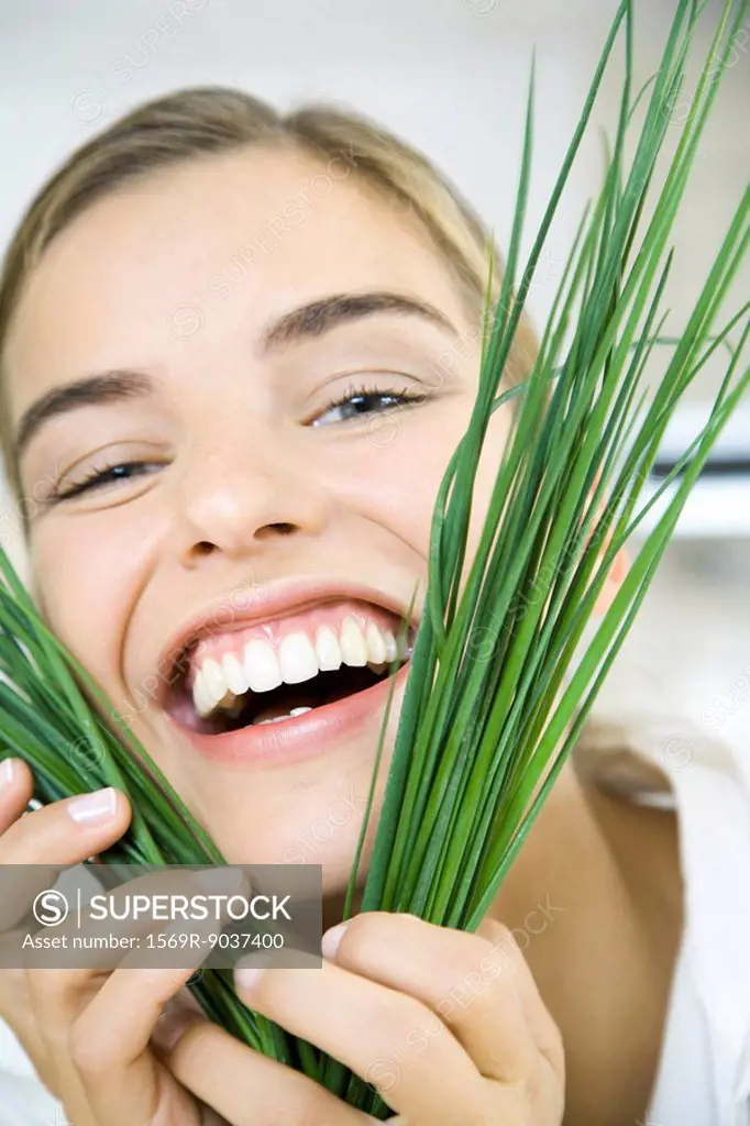 Woman holding chives up to face, smiling, laughing