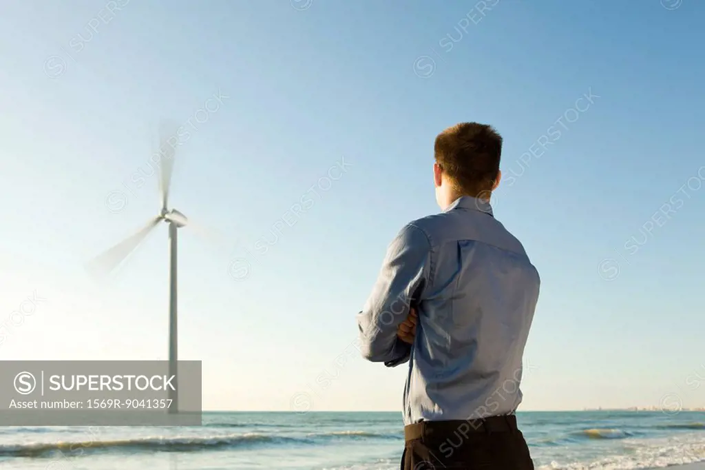 Man on beach observing offshore wind turbine at work