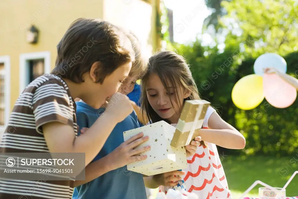 Boy opening gift at birthday party as friends watch