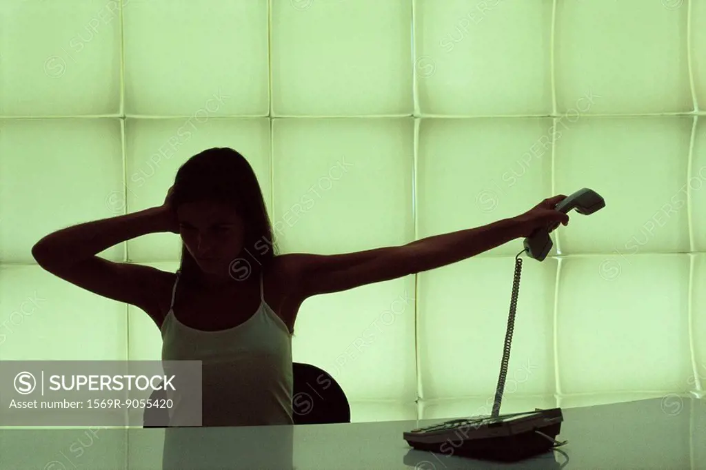 Woman at desk, holding head, holding phone receiver away