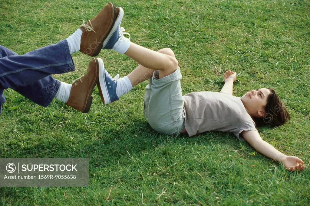 Boy lying on back in grass playing footsies with father