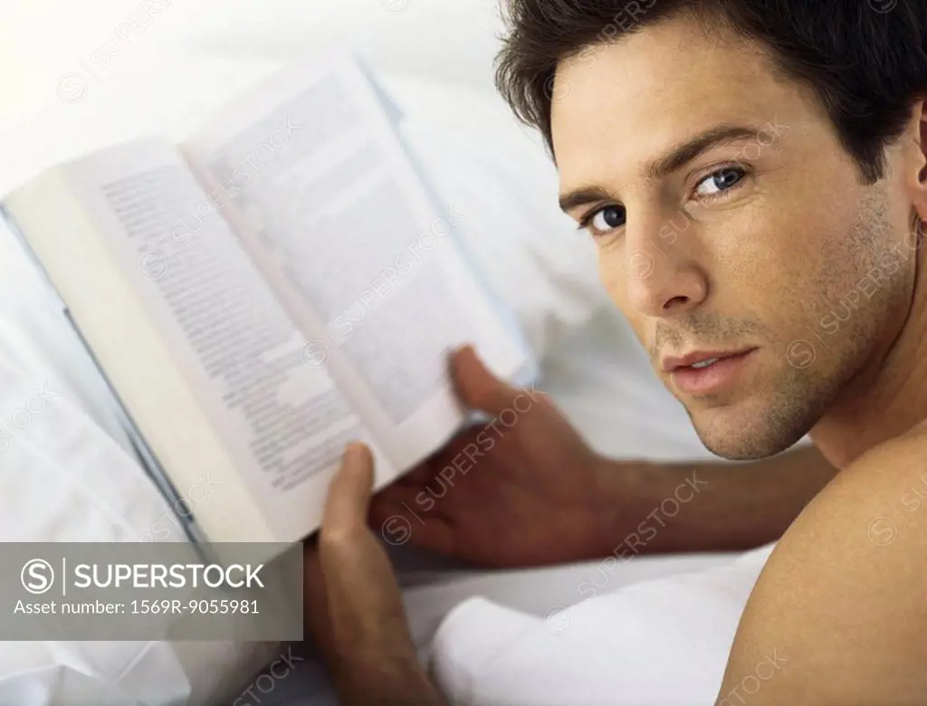 Man holding book, looking over shoulder at camera