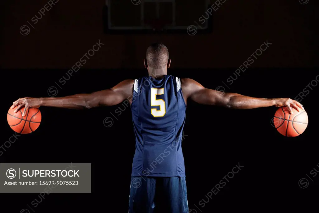 Basketball player holding basketballs in both hands, rear view