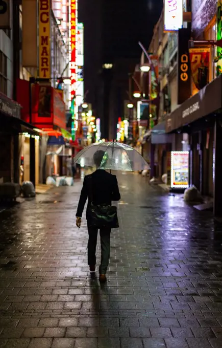 Man walking in rain with umbrella at night