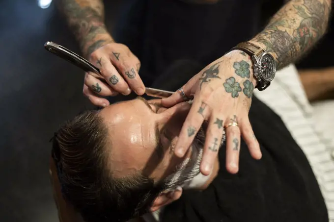 Hairdresser shaving man's beard in salon