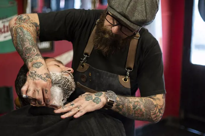 Hairdresser shaving man's beard in salon