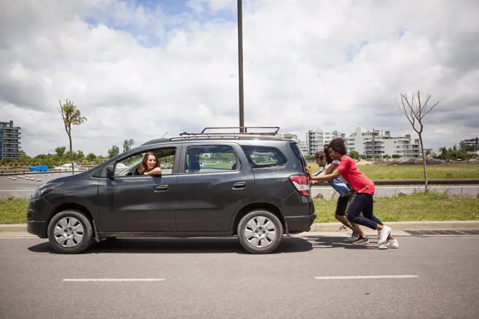 Young friends pushing broken car