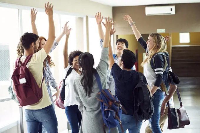 Group of students standing in a circle with hands raised in the air