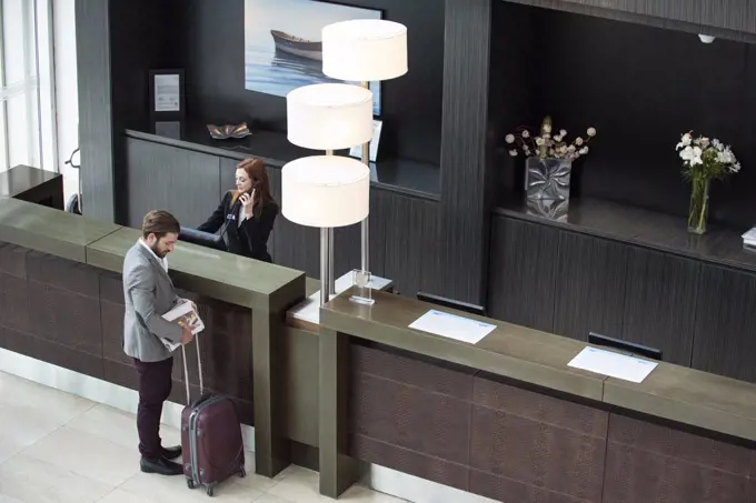 Female receptionist talking on telephone while businessman standing at counter