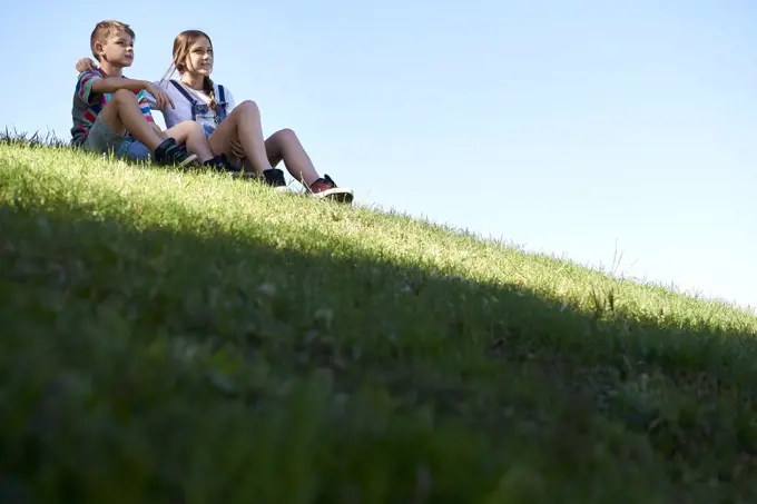 Brother and sister sitting on a grassy hill