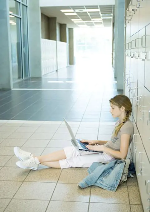 High school girl using laptop in school hallway