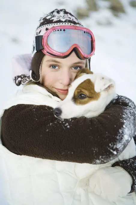 Teenage girl embracing dog, dressed in winter clothing, smiling at camera, portrait