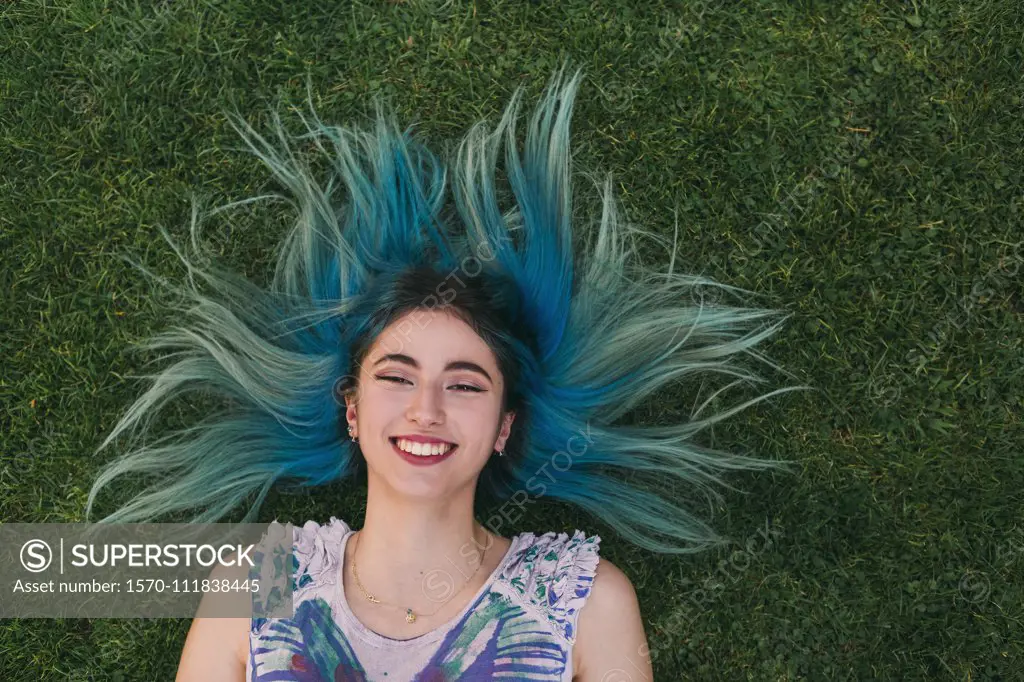 Overhead portrait carefree young woman with blue hair laying in grass