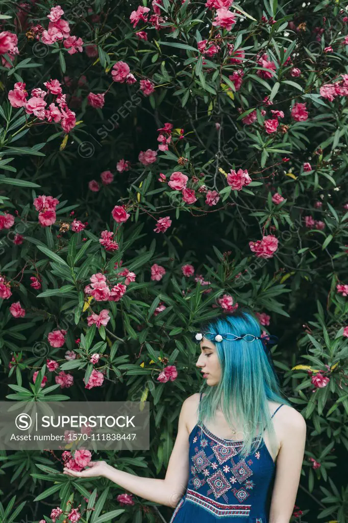 Serene young woman with blue hair standing below flowering tree