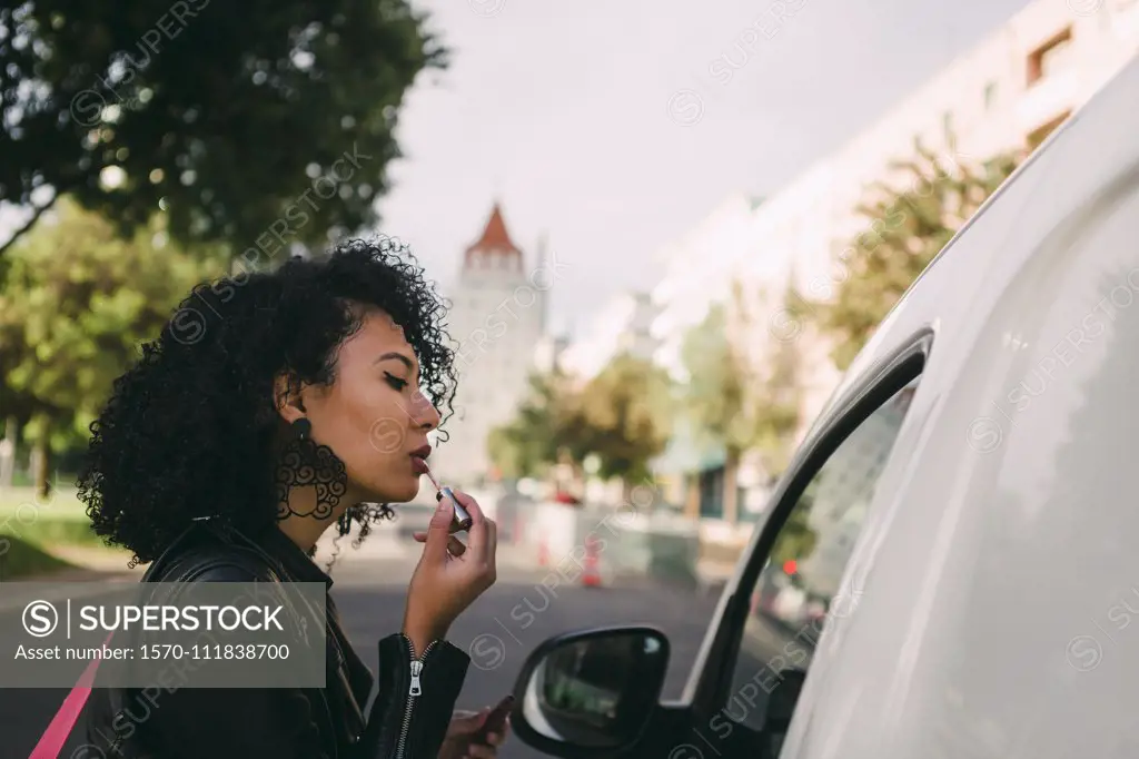 Young woman applying lip gloss in van window