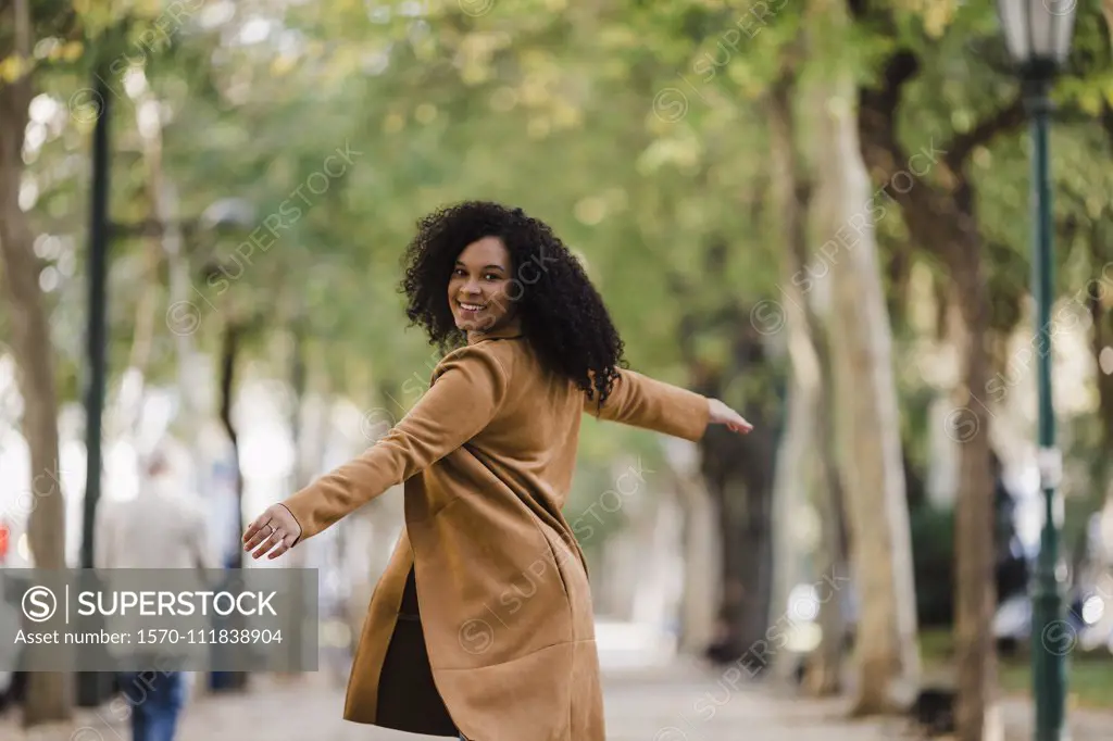 Portrait carefree young woman dancing on treelined sidewalk