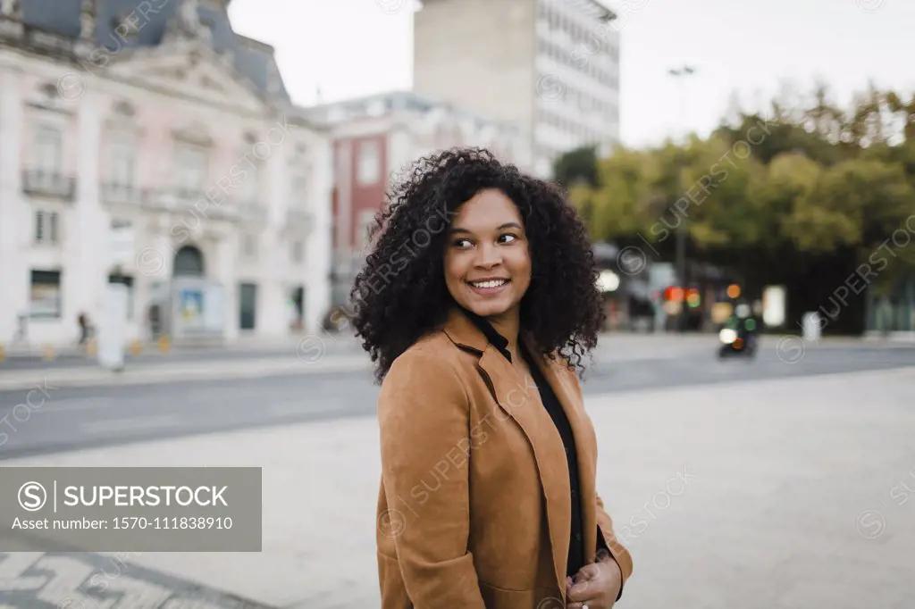 Happy young woman looking over shoulder on urban street