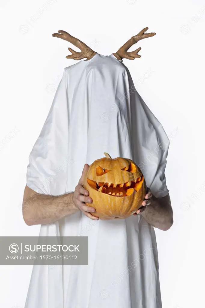 Portrait playful man in sheet costume holding jack o lantern