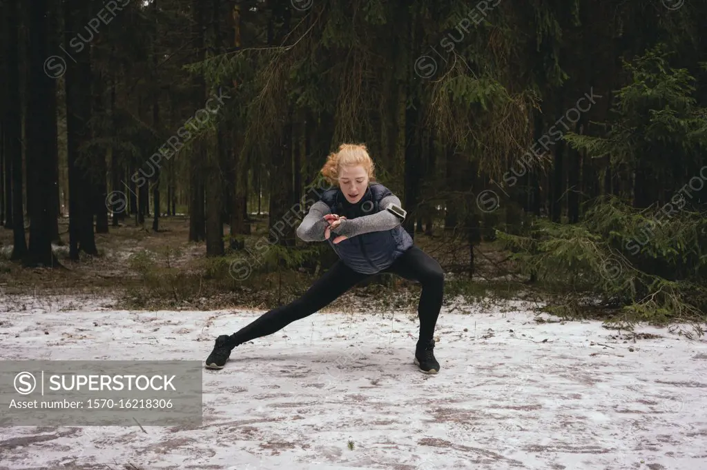 Athletic female runner stretching in snowy woods