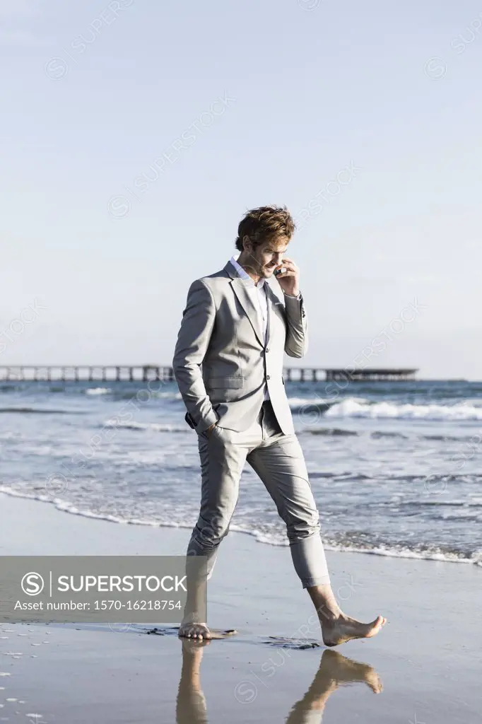 Barefoot businessman walking on sunny ocean beach, Los Angeles, California