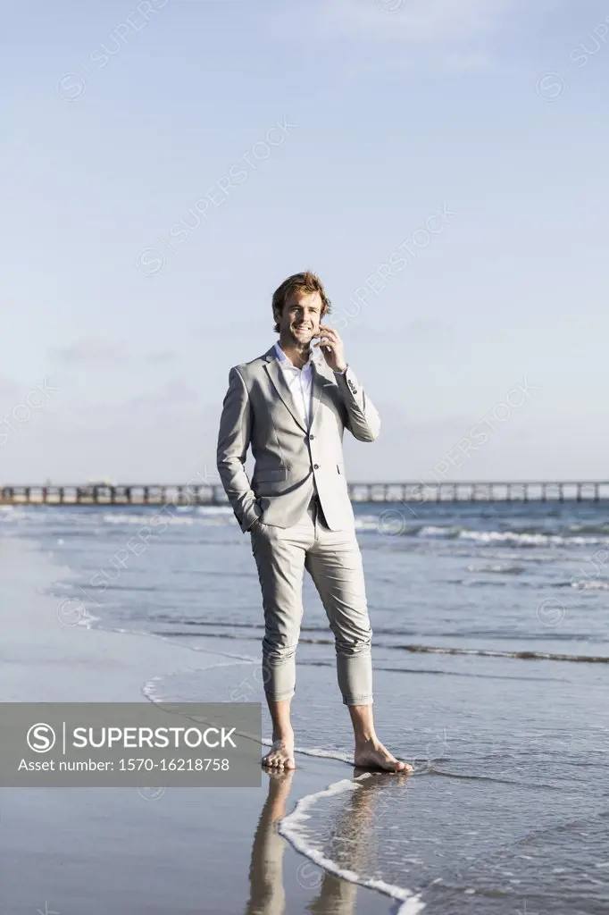 Barefoot businessman talking on smart phone on sunny ocean beach, Los Angeles, California