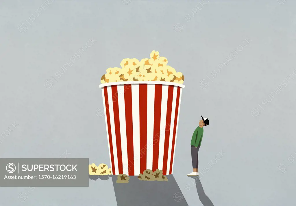 Teenage boy looking up at large movie theater popcorn tub