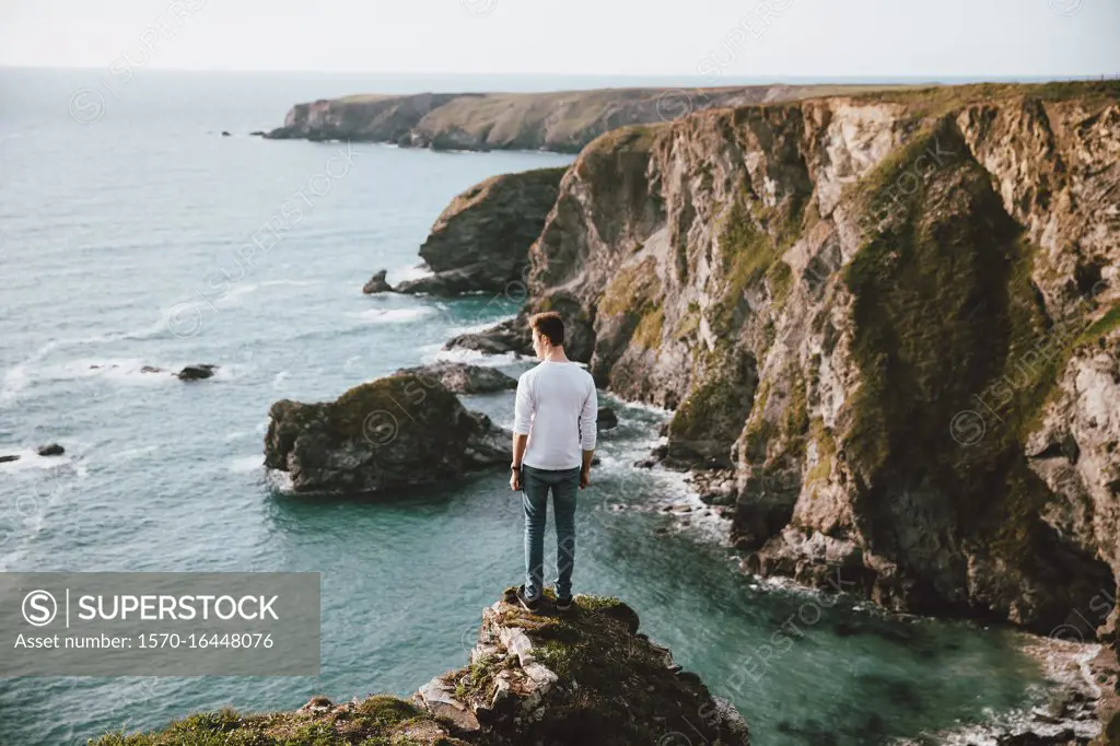 Man standing at edge of cliff over scenic ocean, Bedruthan Steps, Cornwall, UK