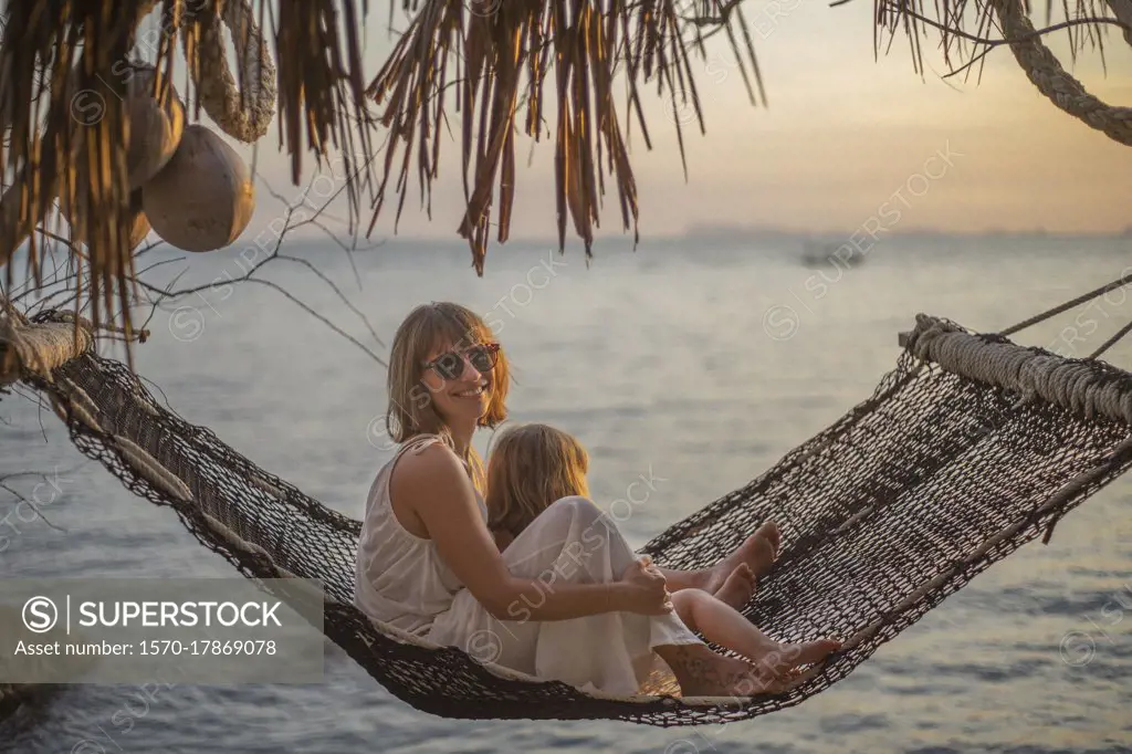 Portrait mother and daughter in hammock enjoying ocean sunset