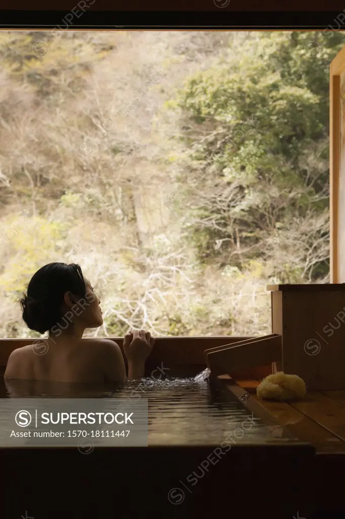 Serene young woman in Onsen pool looking out window