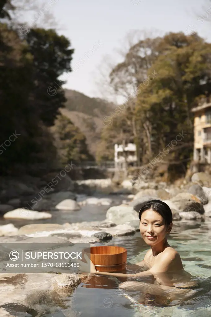 Portrait beautiful young woman with bucket in sunny pool at Onsen