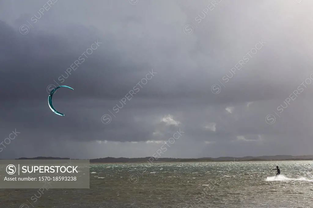 Kite boarder on ocean below stormy cloudy sky