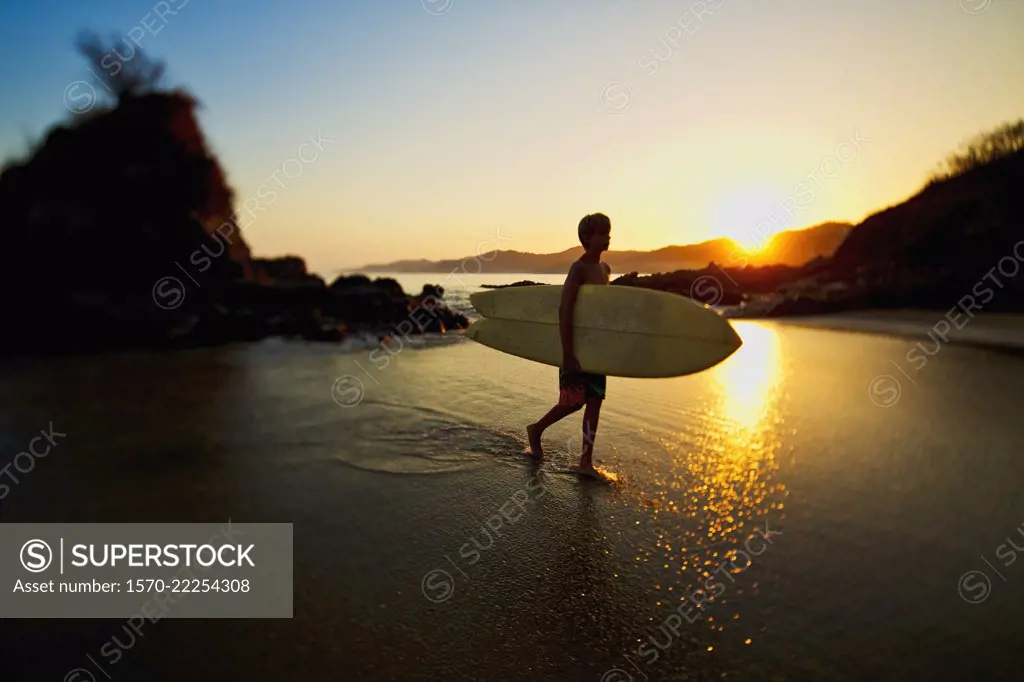 Silhouette boy with surfboard walking on idyllic ocean beach, Sayulita, Nayarit, Mexico