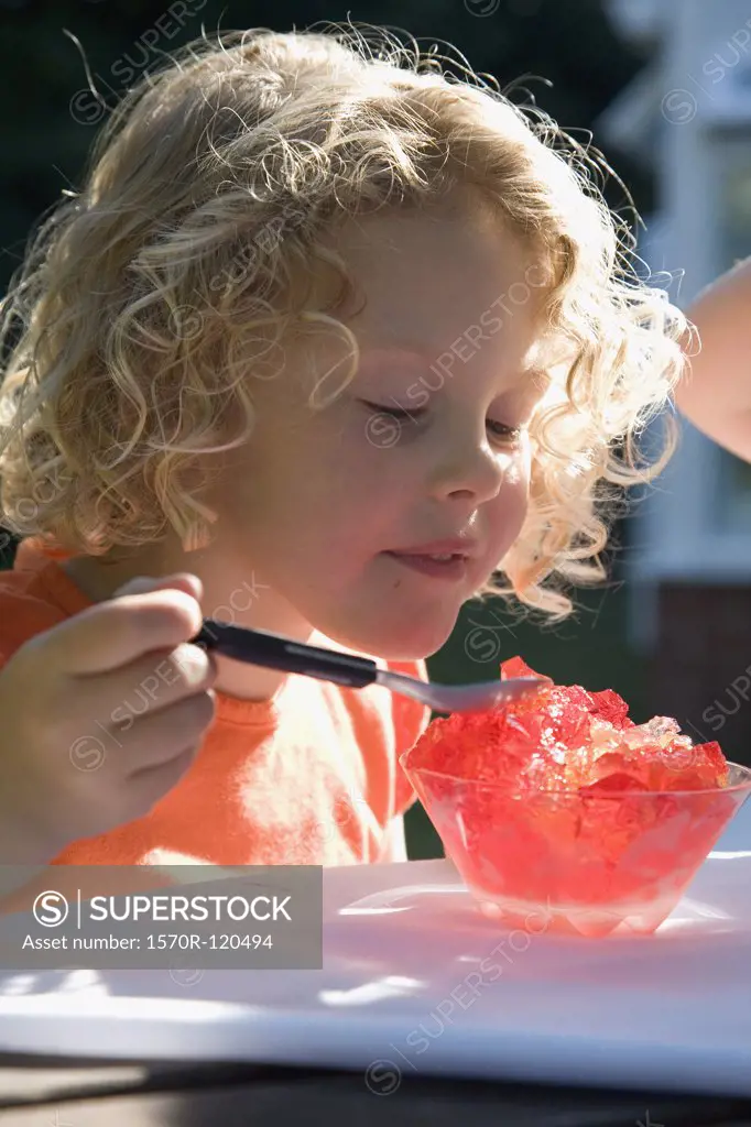 Young girl sitting in a backyard eating jello