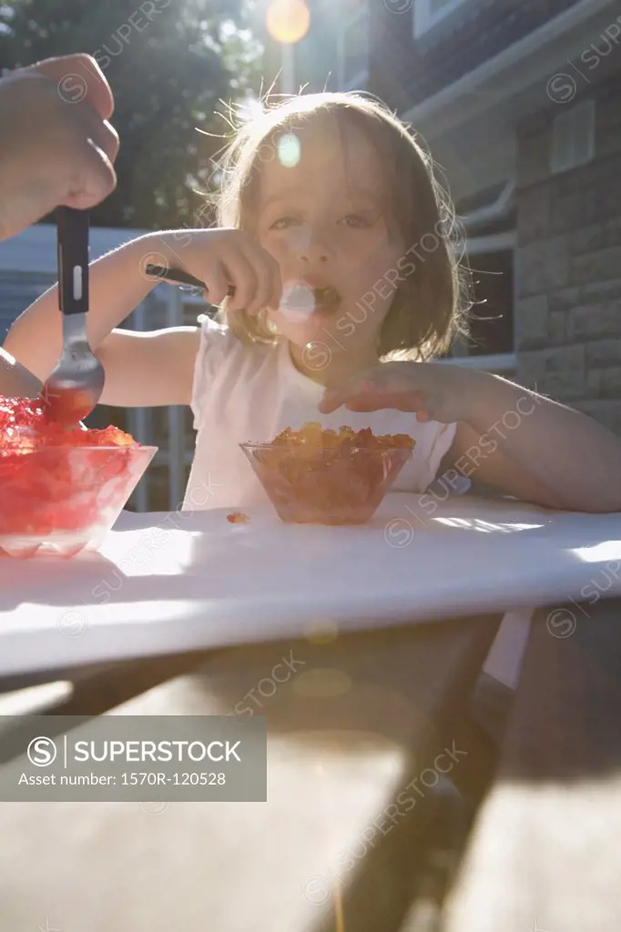 Young girl eating jello at a table in a backyard