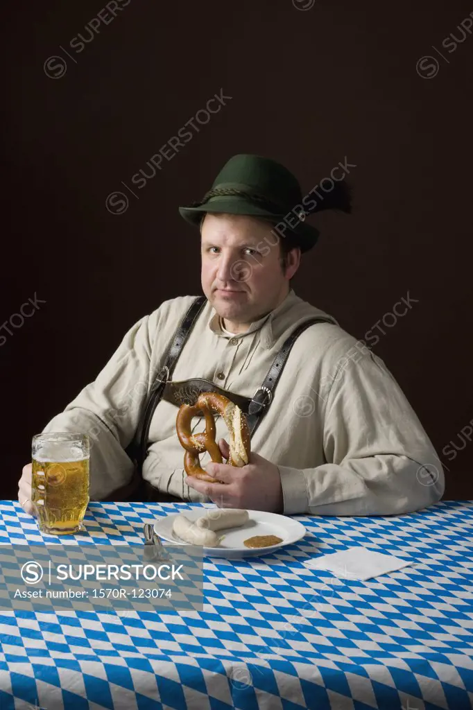 Stereotypical German man in Bavarian costume wiping mouth at a table with a beer and German meal