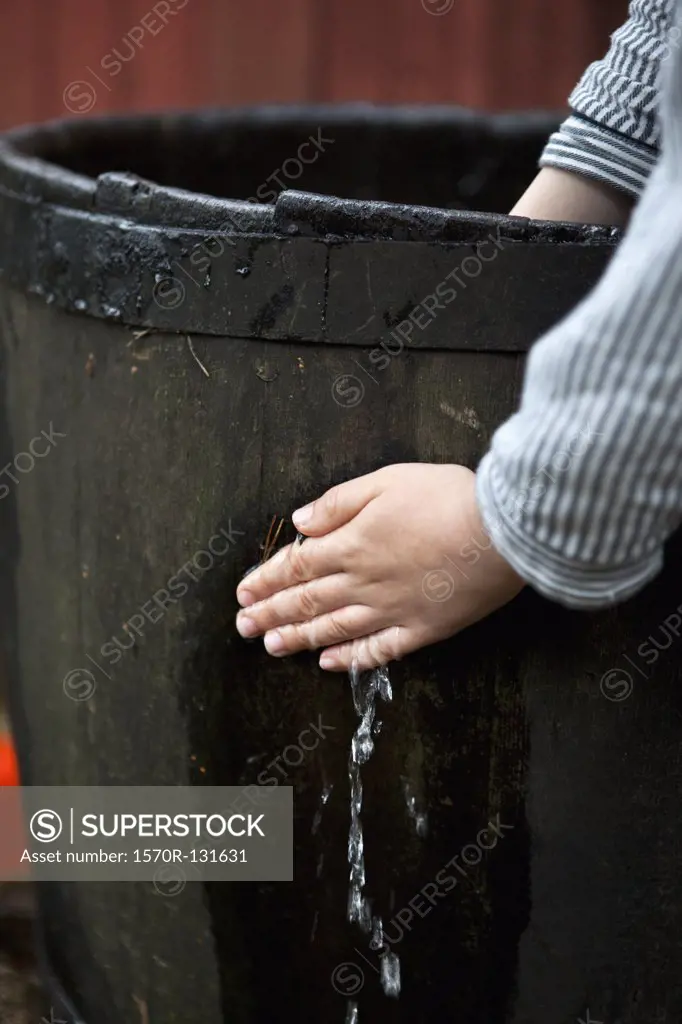 A person stopping water leaking from a wooden barrel