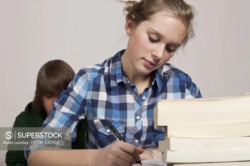 A teenage girl doing class work, boy in background