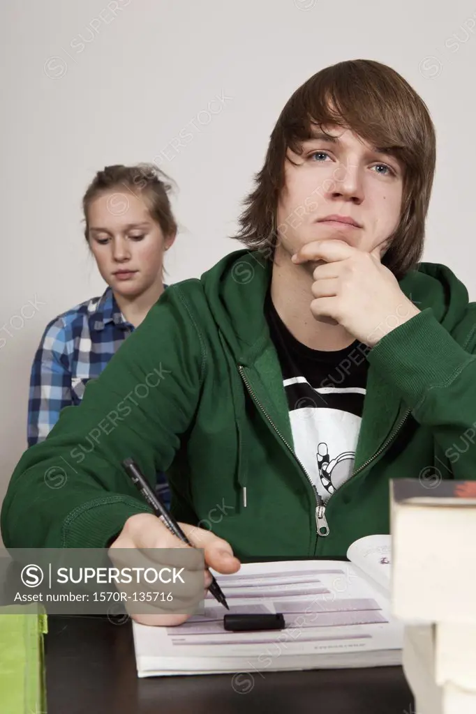 A teenage boy thinking in a classroom, girl in background