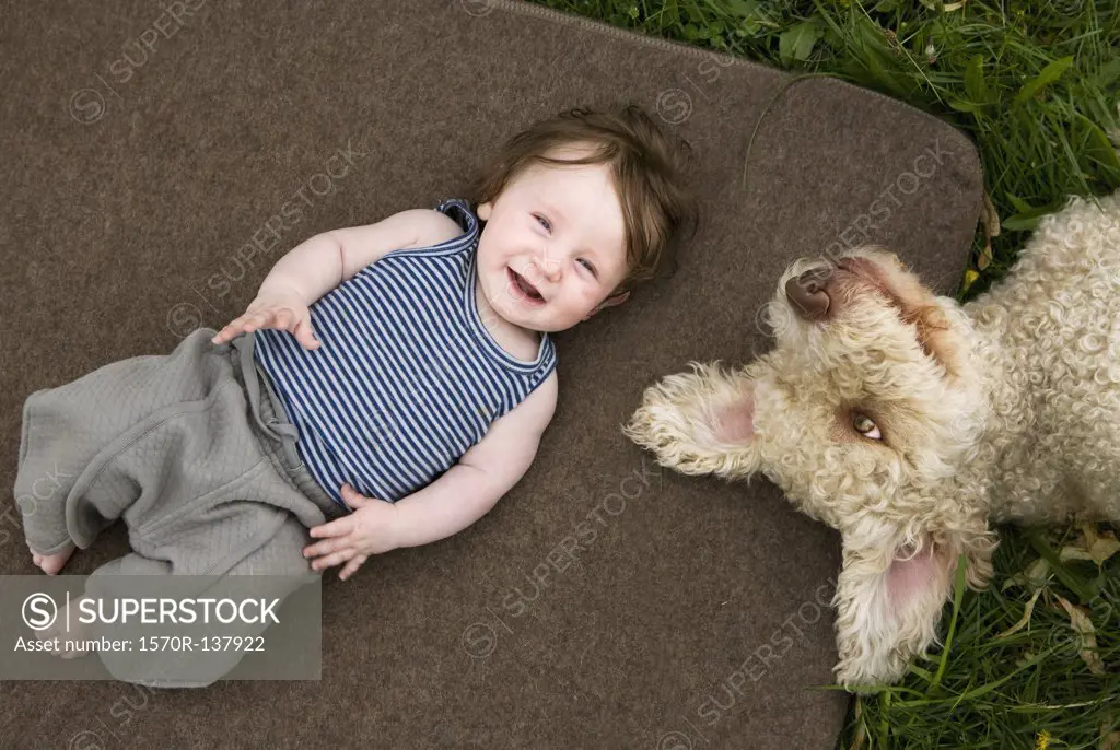 A baby girl and dog lying outside