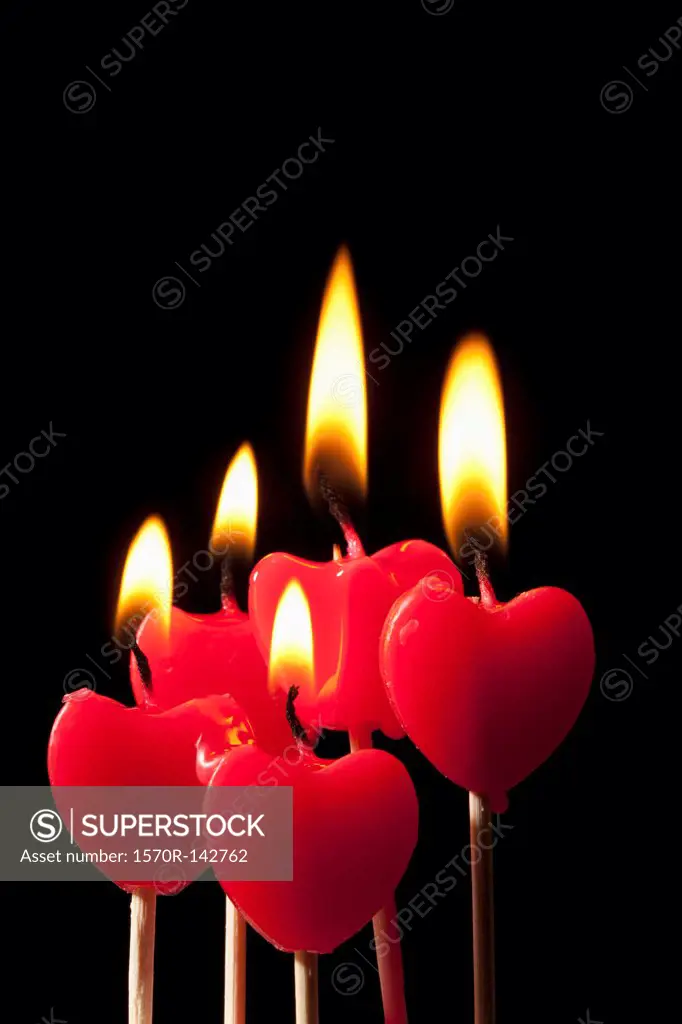 Five lit heart shaped candles on sticks arranged in a group