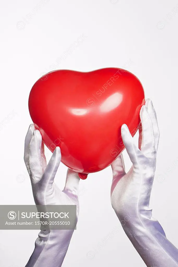 Cropped hands of bride holding heart shape balloon against white background