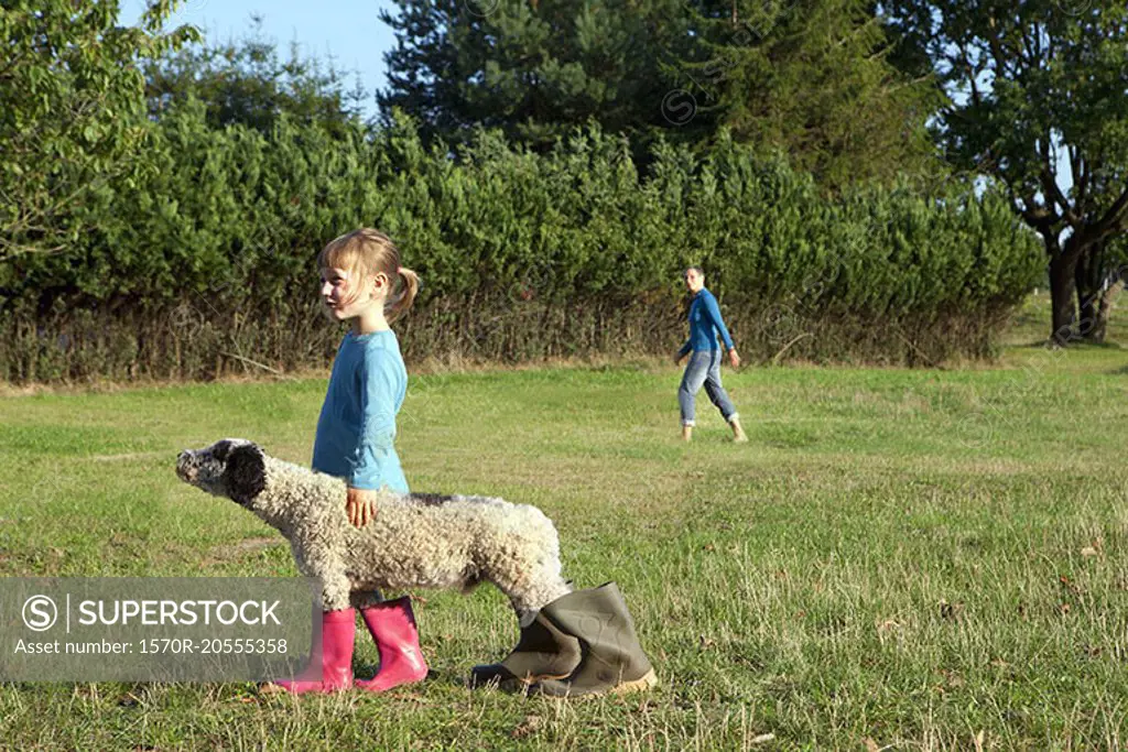 Side view of girl standing with dog wearing rubber boots on field