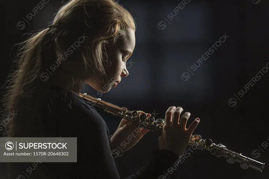 Side view of girl holding flute against black background