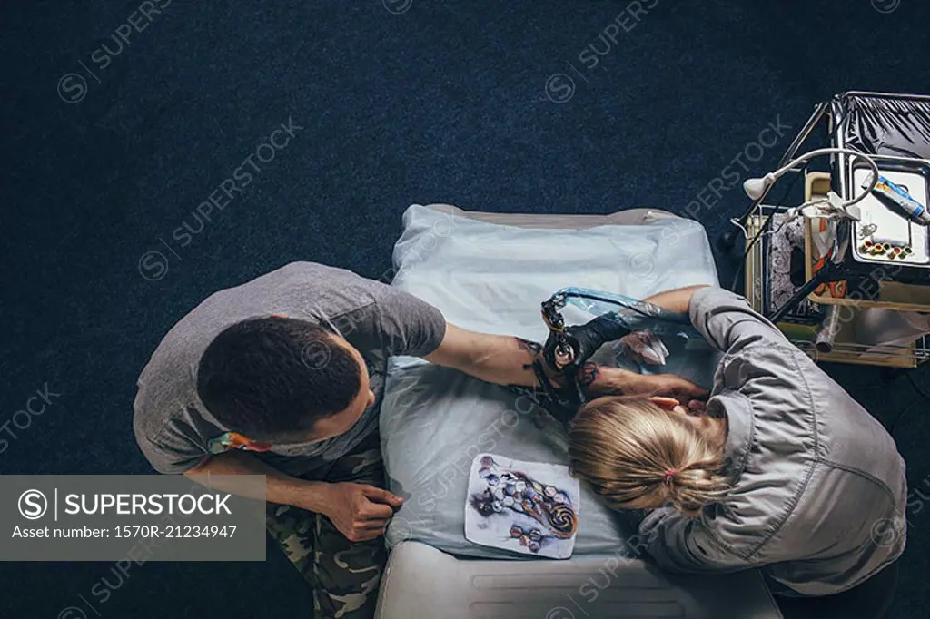 High angle view of tattoo artist tattooing on human hand at studio