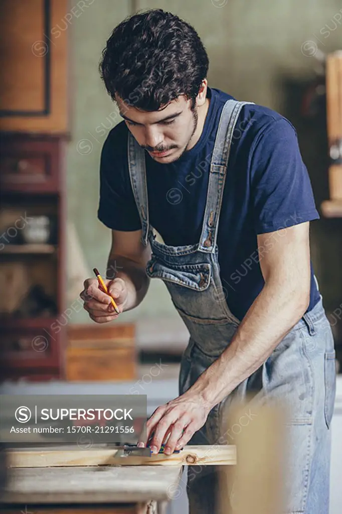 Carpenter marking on wood with pencil and ruler at workshop