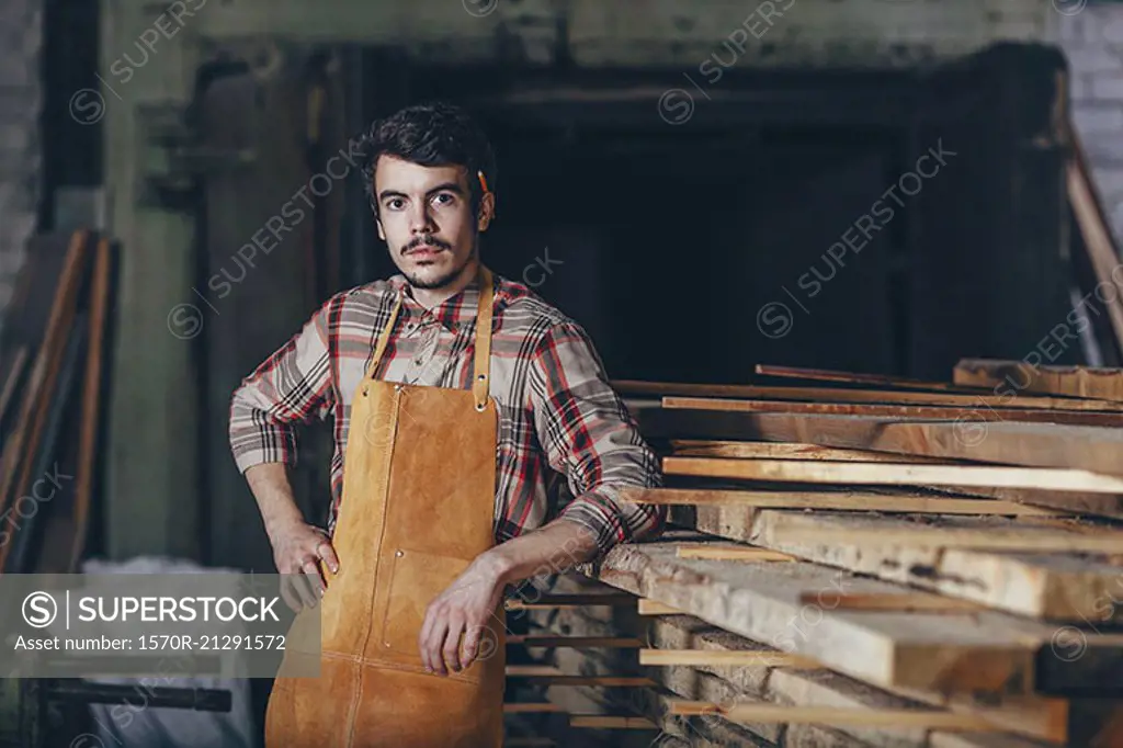 Portrait of carpenter standing by timber stack in workshop