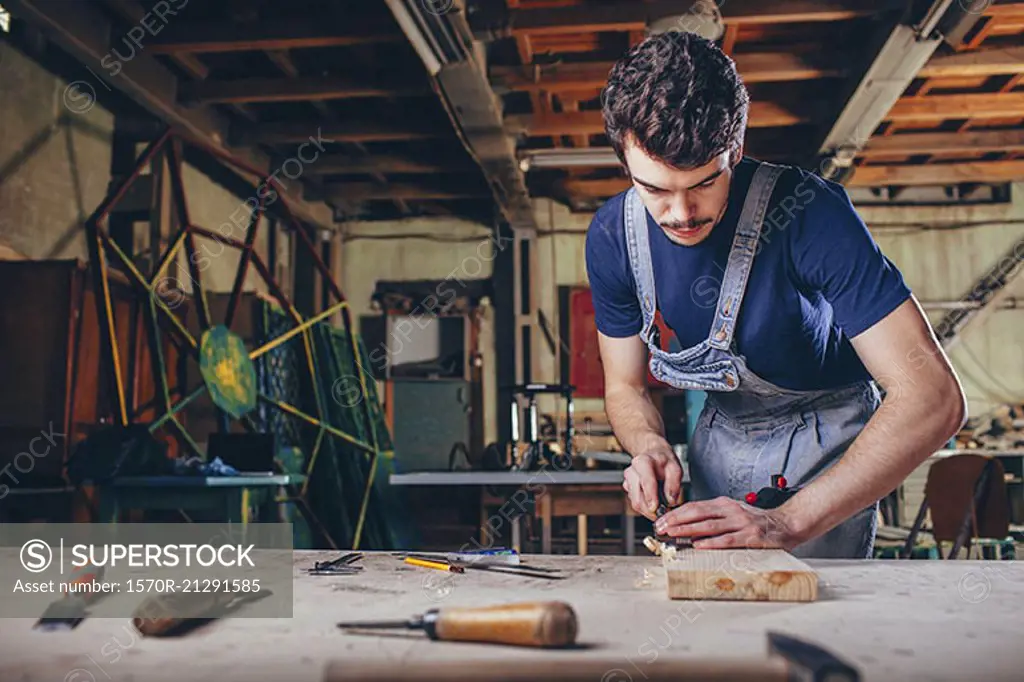 Carpenter using chisel on plank of wood in workshop