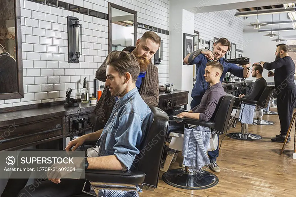 Hairdressers cutting male customer's hair in salon